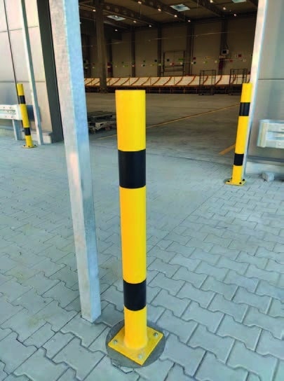 Metalowe odbojnice słupowe w żółto-czarne pasy zamontowane na parkingu przy hali magazynowej